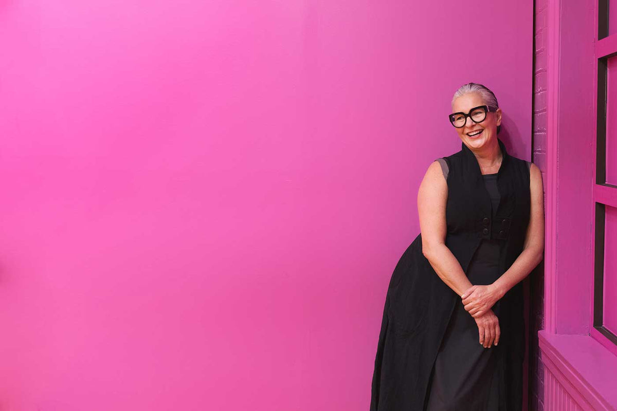 Modern smiling woman in black leaning on a pink background